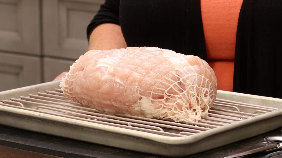 Raw boneless turkey breast in netting on a wire rack over a baking sheet, ready to be seasoned for low roasting.