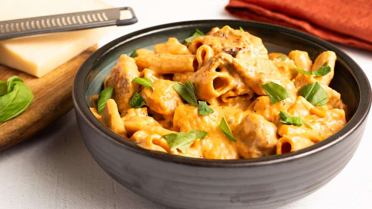 A bowl of One-Pot Marry Me Chicken (Pressure Cooker) with creamy rigatoni pasta, tender chicken pieces, and fresh basil, served next to shaved parmesan and a red napkin.