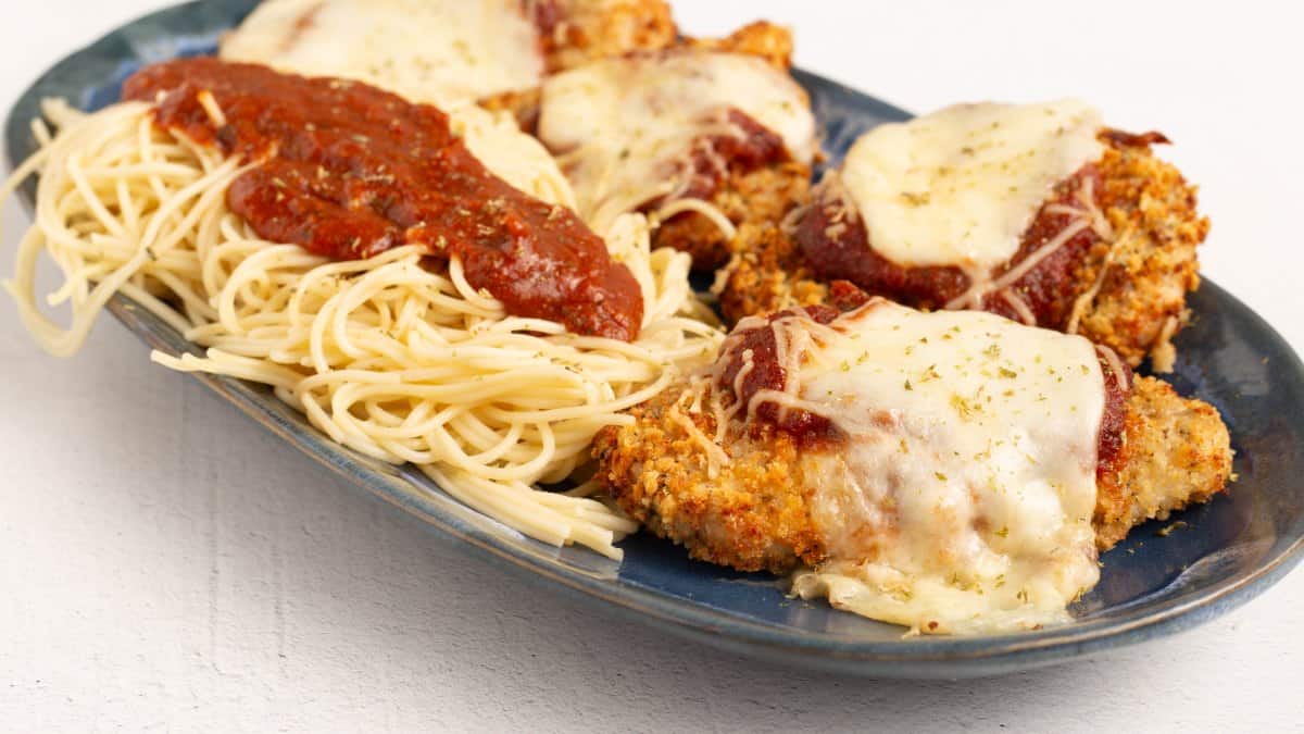 Air Fryer Chicken Parmesan arranged on a blue platter with angel hair pasta, marinara sauce and melted mozzarella over the crispy panko crust.