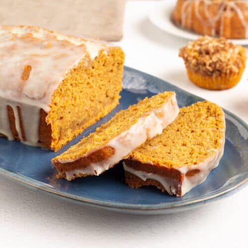 Close view of Glazed Pumpkin Bread slices on a blue platter, the soft pumpkin crumb edged with white chocolate orange glaze.