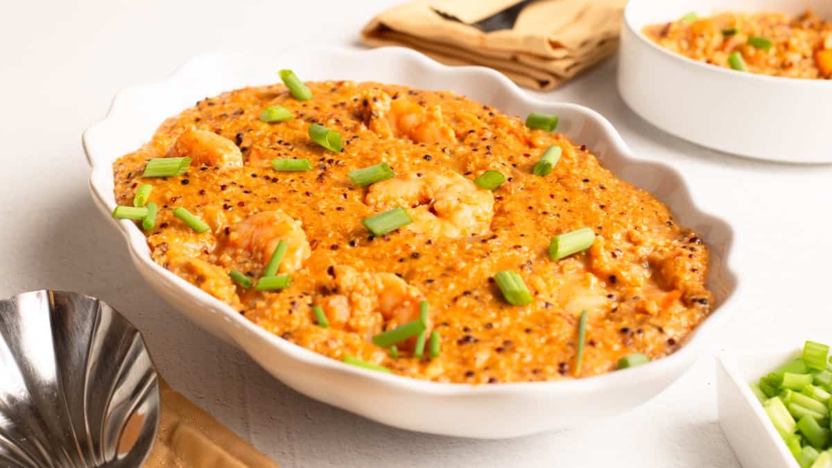 Shrimp & Grits (Possible cooker Pro served in a white scalloped dish, with shrimp and flecks of multicolored quinoa in cheesy orange grits, garnished with green onions.